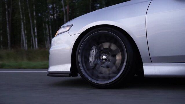 Side view of silver car rides on summer highway. Footage. Perfect auto drives fast on country road. Big sports alloy wheels with powerful brakes