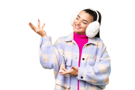 Young woman wearing winter muffs over isolated chroma key background extending hands to the side for inviting to come
