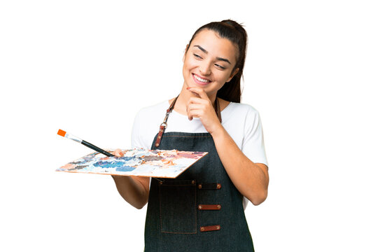Young artist woman holding a palette over isolated chroma key background looking to the side and smiling