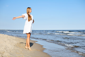 Happy smiling beautiful woman is walking on the ocean beach with open arms