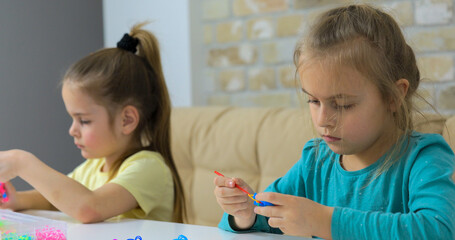 Two girls weaving bracelets made of multicolored rubber bands