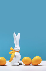 White Easter bunny with yellow ribbon bow with dyed orange eggs on white table. Happy Easter banner with copy space