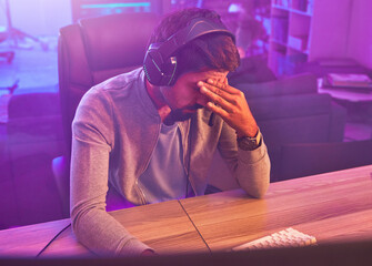 Stress, gamer or man with headache from loss, fail or online competition tournament anxiety in room. Neon, sad or depression male for gaming mental health, live stream disappointment or esport glitch © Courtney H/peopleimages.com