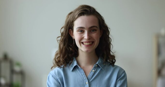 Happy woman having pretty appearance charming smile staring at camera, head shot. Portrait of successful company employee, student girl standing posing indoor. Youth, positive emotions, natural beauty