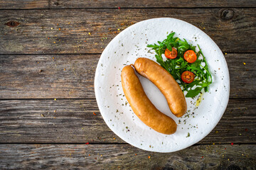 Breakfast - boiled sausages, bread and fresh vegetables served on wooden table
