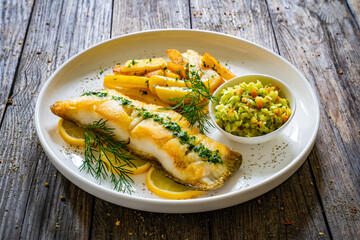 Fish dish - fried cod with French fries and cabbage salad on wooden table