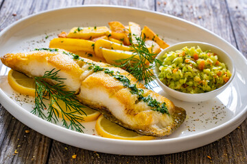 Fish dish - fried cod with French fries and cabbage salad on wooden table
