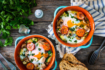 Delicious breakfast - roasted eggs with white mushrooms and vegetable served in oven dish on wooden table
