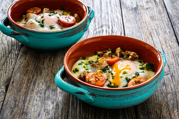 Delicious breakfast - roasted eggs with white mushrooms and vegetable served in oven dish on wooden table
