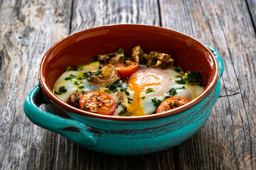 Delicious breakfast - roasted eggs with white mushrooms and vegetable served in oven dish on wooden table
