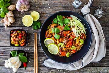Asian food - chicken nuggets, noodles, stir fried vegetables, soy sauce, cabbage and shimeji mushrooms on wooden table
