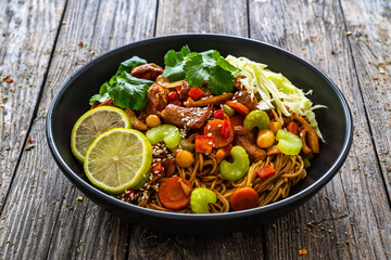 Asian food - chicken nuggets, noodles, stir fried vegetables, soy sauce, cabbage and shimeji mushrooms on wooden table
