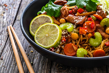 Asian food - chicken nuggets, noodles, stir fried vegetables, soy sauce, cabbage and shimeji mushrooms on wooden table
