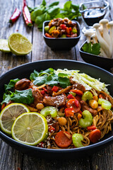 Asian food - chicken nuggets, noodles, stir fried vegetables, soy sauce, cabbage and shimeji mushrooms on wooden table
