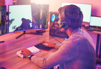 Computer gaming, man and headphones for esports, online games or virtual competition in dark room. Gamer guy, digital player and live streaming on headset in neon lighting, technology or rpg streamer