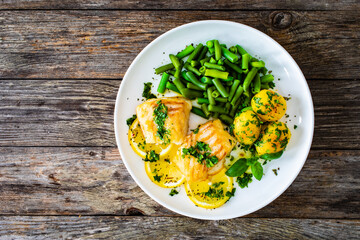 Fish dish - fried halibut with baked potatoes and boiled green beans on wooden table
