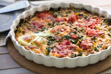 Egg, spinach, and tomatoes gratin in a large baking dish on a rustic table
