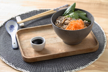 Shiitake mushrooms and soba noodle soup with carrot, spinach, and soy sauce on a wooden tray