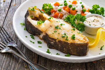 Fish dish - fried halibut with white rice, peas and carrots on wooden table
