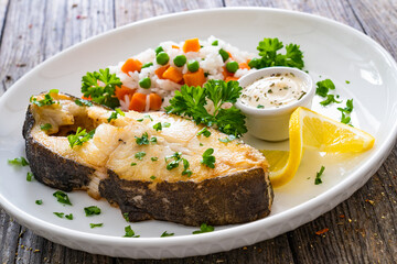 Fish dish - fried halibut with white rice, peas and carrots on wooden table
