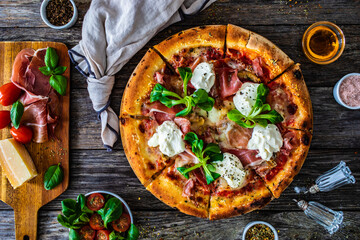 Circle prosciutto pizza with mascarpone cheese and leafy greens on wooden table
