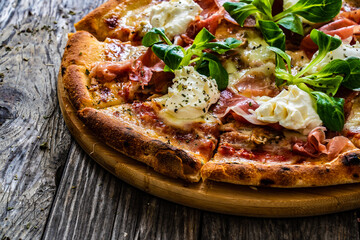 Circle prosciutto pizza with mascarpone cheese and leafy greens on wooden table
