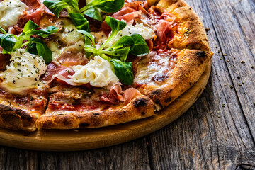 Circle prosciutto pizza with mascarpone cheese and leafy greens on wooden table
