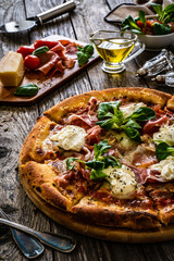 Circle prosciutto pizza with mascarpone cheese and leafy greens on wooden table
