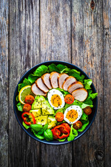 Tasty salad - roasted veal loin, avocado, boiled eggs and fresh vegetables on wooden table

