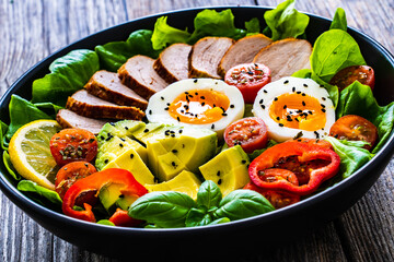 Tasty salad - roasted veal loin, avocado, boiled eggs and fresh vegetables on wooden table
