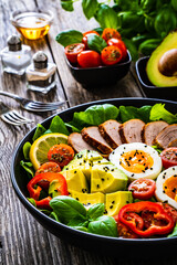 Tasty salad - roasted veal loin, avocado, boiled eggs and fresh vegetables on wooden table
