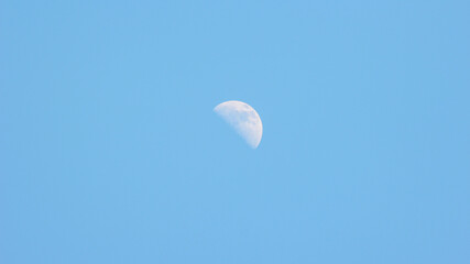 A crescent moon in the blue sky during the day.