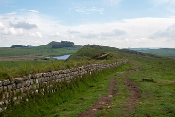 Fototapeta na wymiar Views of Crag Lough in Northumberland National Park, against foreground of Whin Sill rocky crags and Hadrian's Wall 