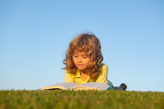Boy child reading book, lying down on green grass. Kids adventure, freedom and carefree children.