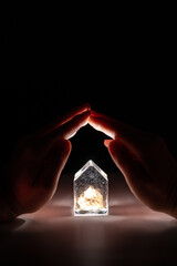 Hands close the crystal house. The concept of protection, reliability and support