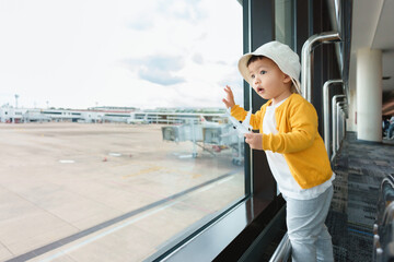 Obraz premium Asian Japanese Little child boy looking through window for airplane at international airport. Traveling.