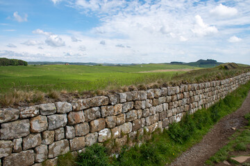 Fototapeta na wymiar A section of Hadrian's Wall close to Milecastle 39 (Roman military base) and adjacent to a footpath route. in Northumberland National Park. With blue cloudy skies during summer 2022