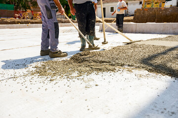 Riggers, workers use rake and handmade wooden tool to level fresh concrete into building foundation...