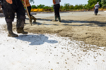 Riggers, workers use rake and handmade wooden tool to level fresh concrete into building foundation