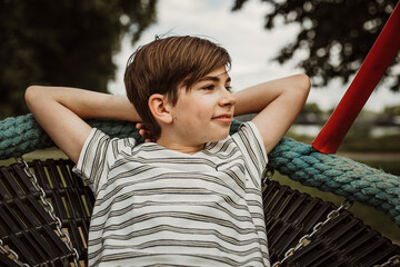 young child boy lie on spider web tree swing on ropes with arms behin head and look do right side...