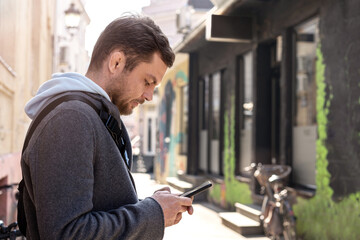Man standing on street and using his phone, typing text, online messaging.