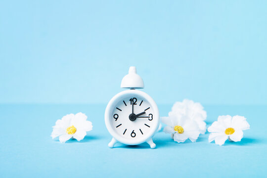 White Alarm Clock and Spring Daisy Flowers on Blue Background