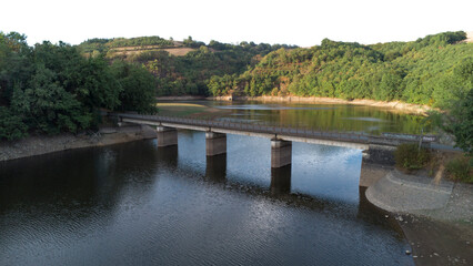 Fototapeta na wymiar Panoramic view of a bridge crossing a lake in summer, surrounded by the green forest and fields.