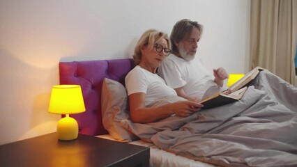 Senior couple read books in bed. Realtime - Powered by Adobe