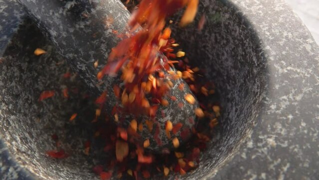 Close-up of the red hot chilli peppers falling into the stone mortar