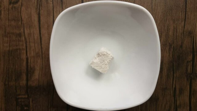 Top view of soft feta cheese cube placed into white bowl with kitchen knife 