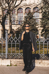 Fototapeta na wymiar Attractive woman walking at the city on the street. Tourist woman walking at old cozy street. Girl wear grey suit and t-shirt, black pants and sunglasses. Street style, fashion look, minimalistic look