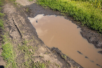 A close-up view of puddles of water on a muddy country road with a track