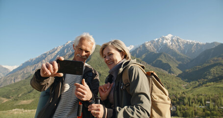 Fototapeta na wymiar Senior caucasian couple having a nordic walk in mountains, then stopping to take a picture with smartphone. Old people travelling together after retirement - pension, tourism concept 
