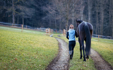 Rider on the way to the pasture with her horse, horse and man on the right, landscape format..